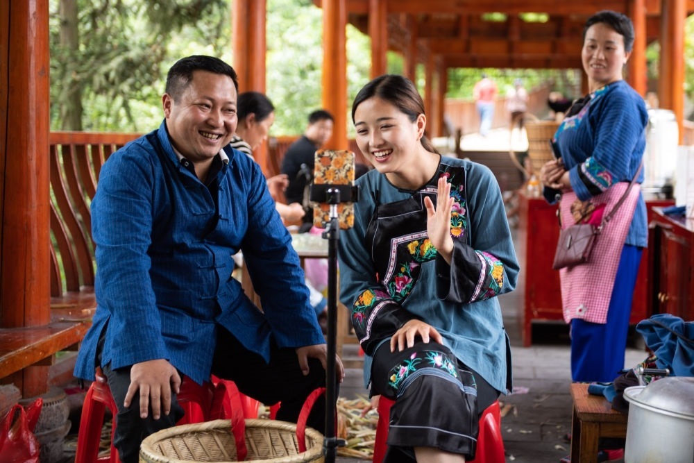 在湖南省湘西土家族苗族自治州花垣縣十八洞村，十八洞村扶貧隊長麻輝煌（左）與返鄉(xiāng)大學生施林嬌（中）一起直播推銷土特產(chǎn)（2020年5月15日攝）。新華社記者 陳思汗 攝