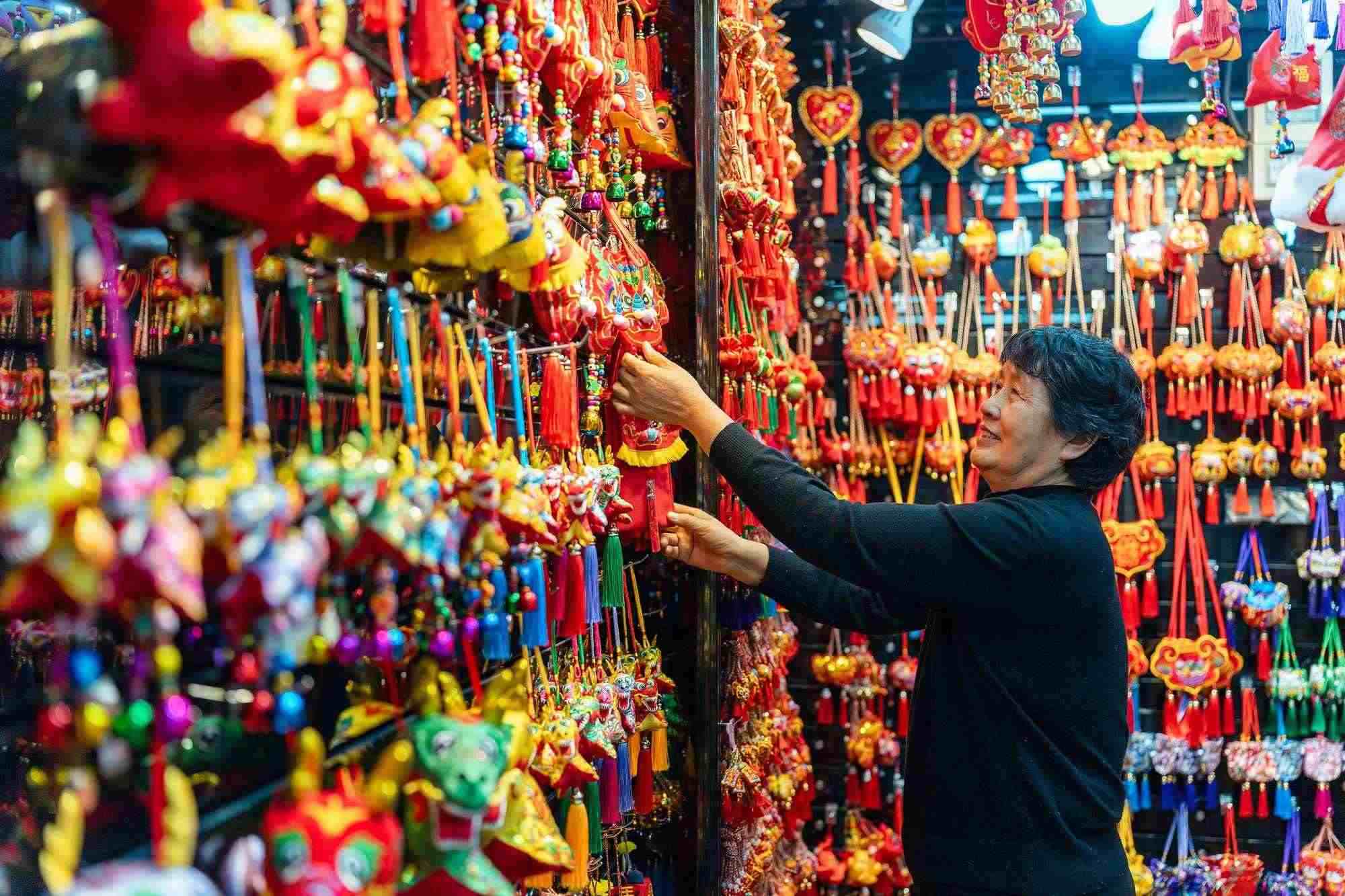 2023年12月11日，金華義烏國際商貿(mào)城，龍年喜慶用品掛滿攤位，顧客正在挑選中。
