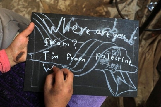 2023年12月28日，一名學(xué)生在加沙地帶南部城市拉法一所學(xué)校的臨時(shí)教室中寫下“我來自巴勒斯坦”的字樣。新華社發(fā)（里澤克·阿卜杜勒賈瓦德攝）