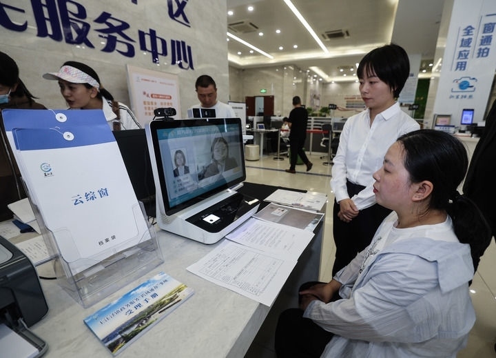 在浙江省嘉興市秀洲區(qū)王江涇鎮(zhèn)便民服務(wù)中心的“跨域通辦·云綜窗”窗口，辦理開業(yè)登記的個(gè)體工商戶（右一）通過該系統(tǒng)與江蘇省蘇州市吳江區(qū)盛澤鎮(zhèn)行政審批局工作人員視頻連線，進(jìn)行身份讀取及材料線上審核（2024年5月9日攝）。新華社記者 徐昱 攝