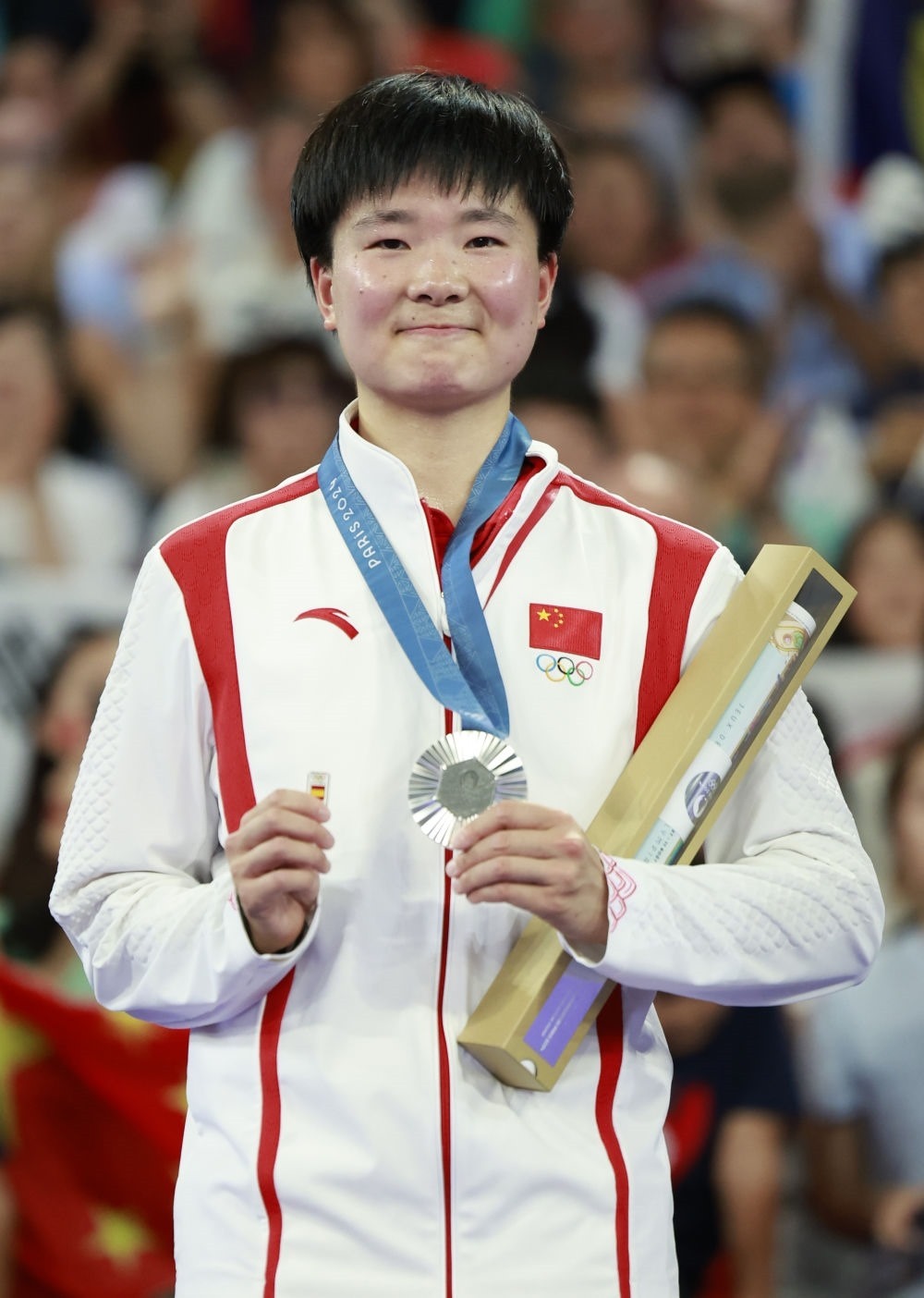巴黎奧運(yùn)會(huì)羽毛球女子單打亞軍、中國(guó)選手何冰嬌在頒獎(jiǎng)儀式上一手握著銀牌，一手握著西班牙奧委會(huì)徽章（2024年8月5日攝）。新華社記者 任正來(lái) 攝