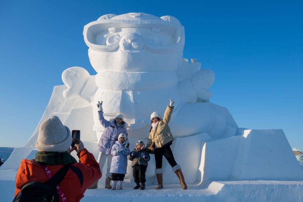 2025年1月3日，在黑龍江哈爾濱冰雪大世界園區(qū)，游客與亞冬會吉祥物雪雕“濱濱”合影